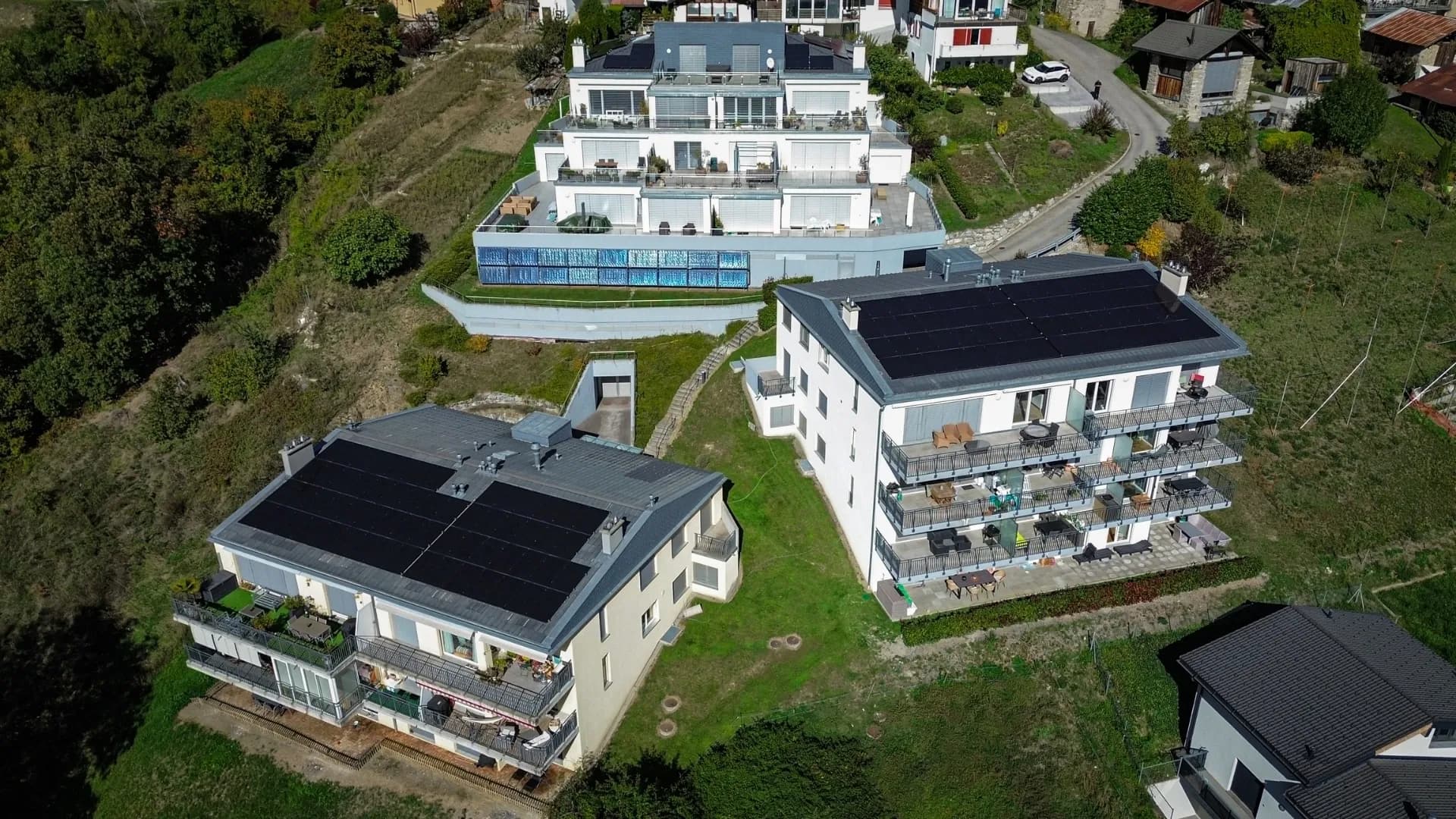Vue drone de trois bâtiments résidentiels équipés d’installations solaires à Savièse, au cœur des montagnes valaisannes.